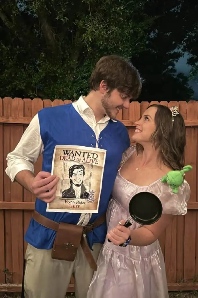 Couple dressed as Rapunzel and Flynn Rider from Tangled for Halloween. Rapunzel costume includes a lavender dress, tiara, Pascal accessory, and frying pan prop. Flynn Rider costume features a blue vest, white shirt, belt, and wanted poster.