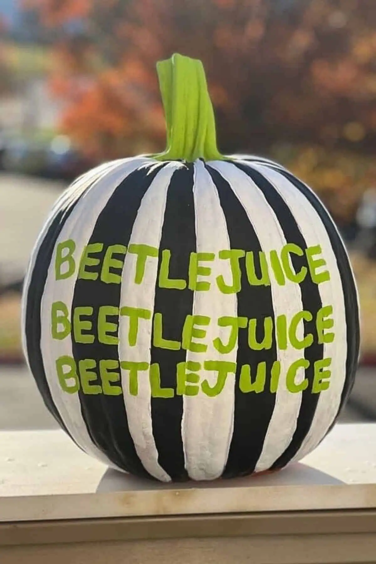 No-carve Halloween pumpkin painted with bold black and white Beetlejuice-style stripes and neon green “Beetlejuice” lettering, inspired by the classic film. Creative and easy DIY pumpkin decorating idea for fall or Halloween porch decor.