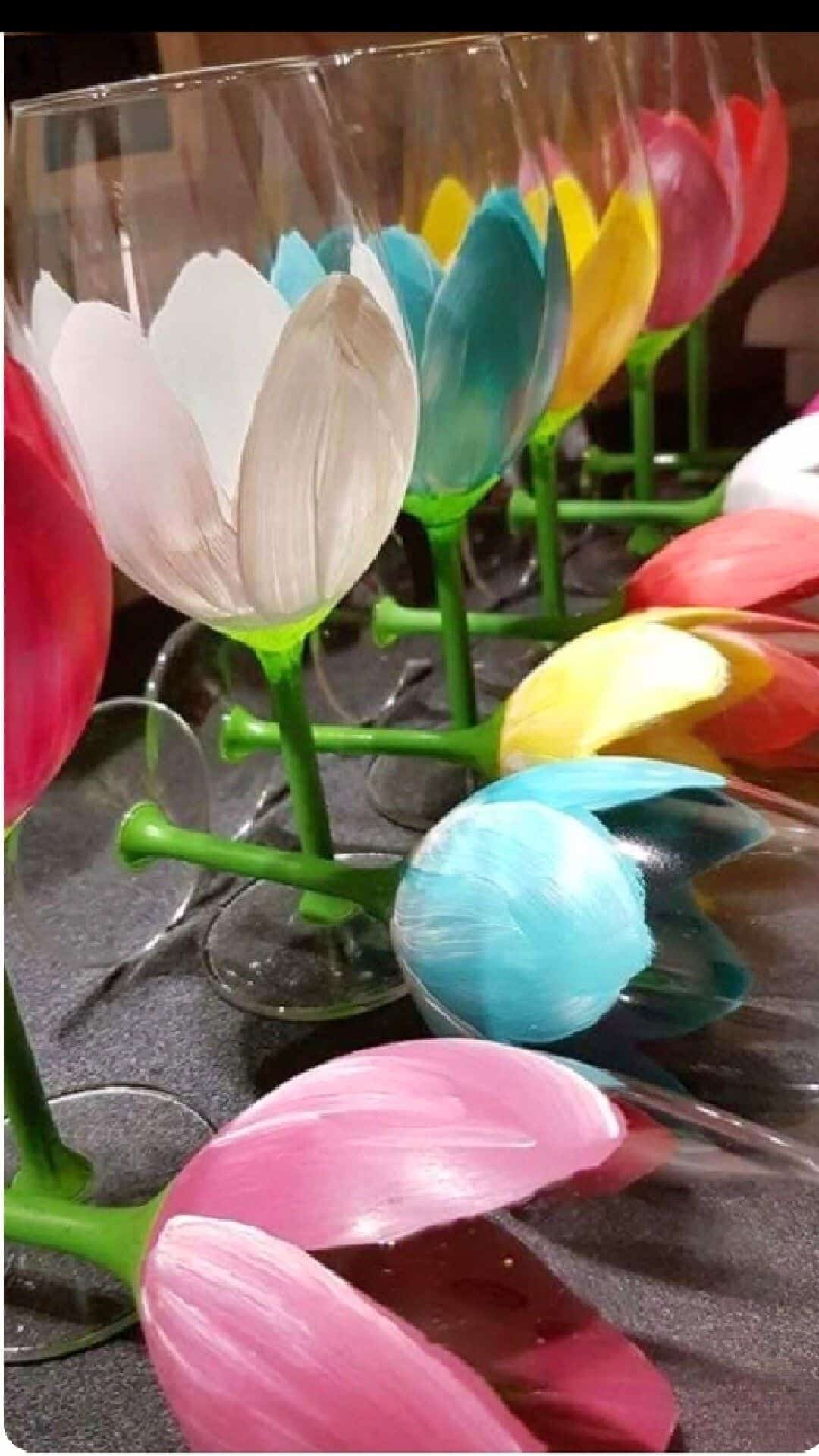 Upside down painted wine glasses transformed into colorful tulip-shaped flowers with green stems, displayed in rows as a vibrant DIY summer craft.