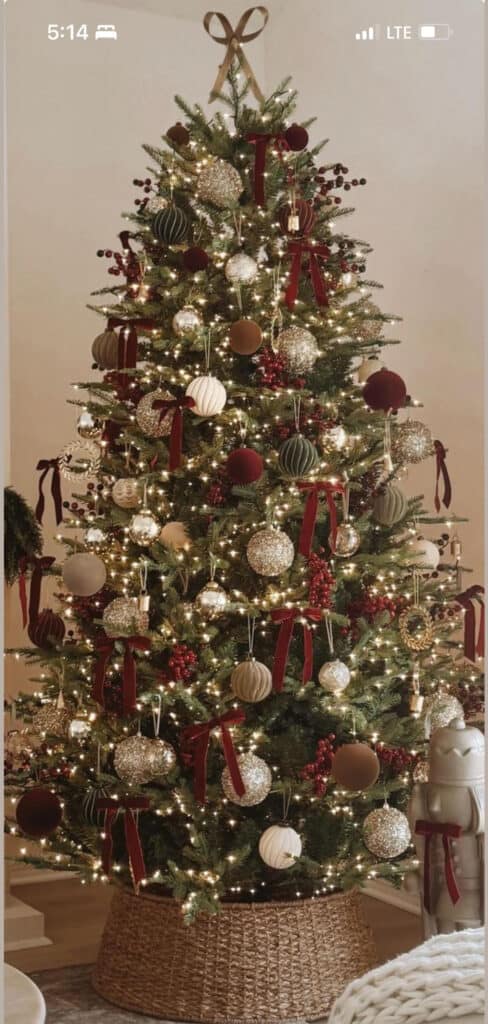 Traditional luxury Christmas tree decorated with burgundy ribbons, gold and champagne ornaments, berry sprigs, and warm white lights in a woven basket base