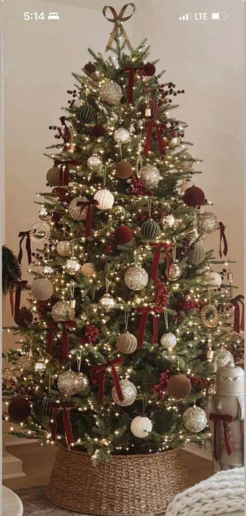 Traditional luxury Christmas tree decorated with burgundy ribbons, gold and champagne ornaments, berry sprigs, and warm white lights in a woven basket base