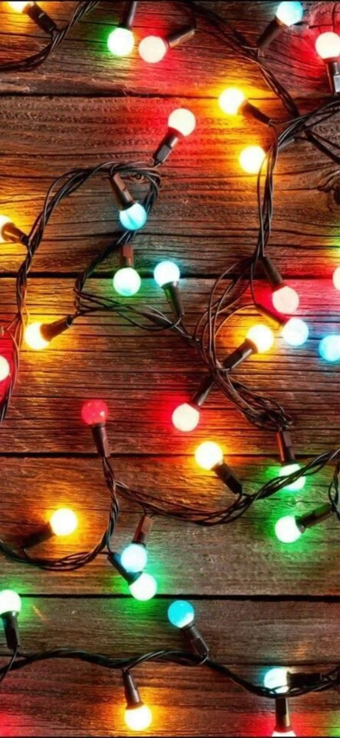 Colorful Christmas string lights glowing against a rustic wooden background. Red, green, yellow, and blue bulbs create a cozy and festive holiday atmosphere, perfect for Christmas decor or wallpaper.