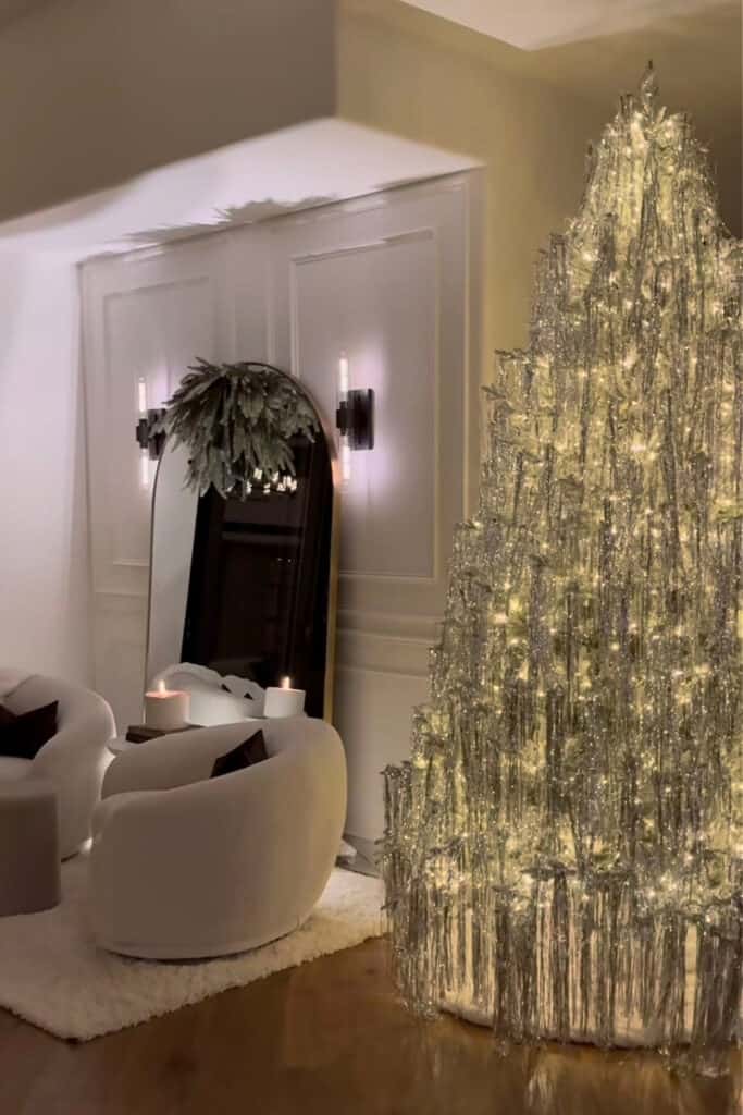 Elegant living room decorated with a retro-inspired silver tinsel Christmas tree illuminated with warm white lights — cozy and glamorous holiday decor setup.