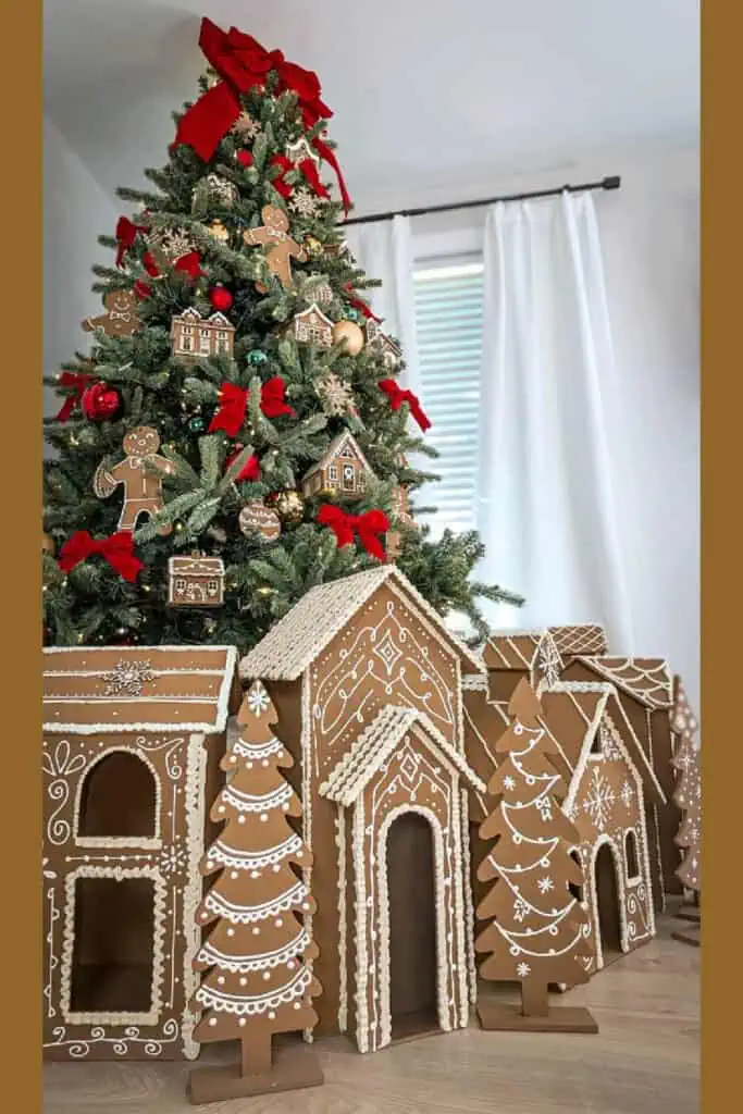 Christmas tree decorated with gingerbread ornaments, red bows, and a display of cardboard gingerbread houses at the base, creating a cozy holiday village theme.