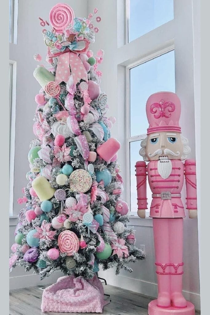 Candyland Christmas tree decorated in pastel pink, blue, and mint ornaments with lollipops, candy-themed decorations, and a large pink nutcracker standing beside it.