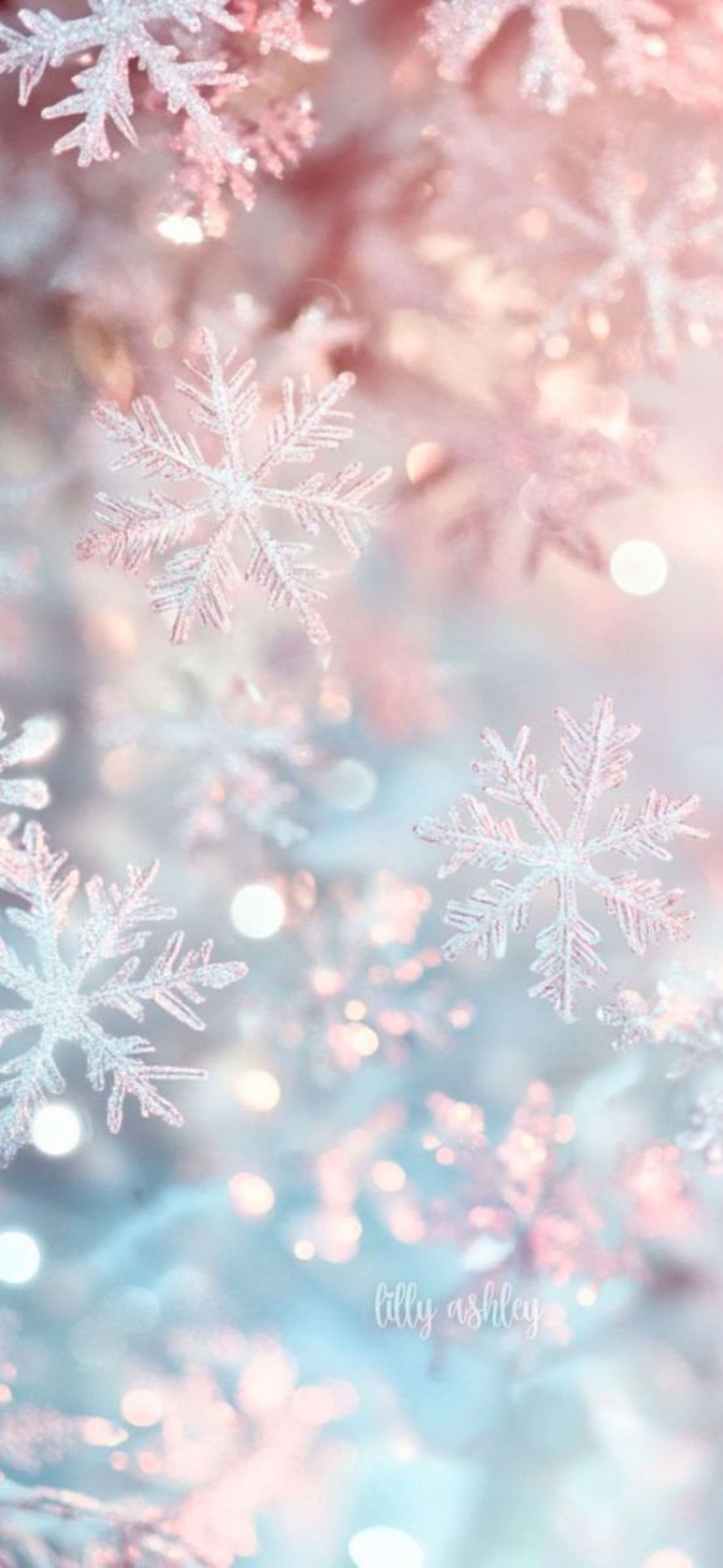 Close-up of delicate pastel snowflakes sparkling against a soft pink and icy blue background, creating a dreamy winter and Christmas aesthetic with bokeh light effects.
