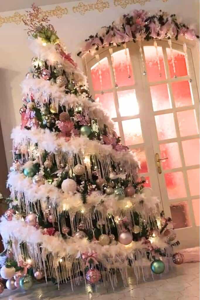 Pastel theme Christmas tree decorated with soft pink, mint green, and pearl ornaments, white feather garlands, and icicle accents, illuminated by warm white lights for a dreamy, elegant holiday look.