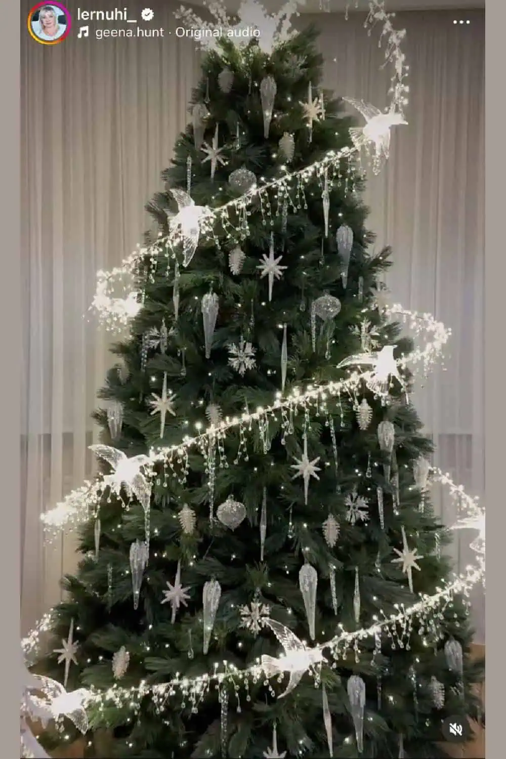 A tall Christmas tree decorated with spiral lights wrapped evenly around the branches, featuring glowing bird-shaped ornaments, icicle drops, silver stars, and shimmering crystal-like decorations. The spiral design creates a clean, elegant look, making this tree perfect for modern or glam holiday themes. A top trend for Christmas 2025.