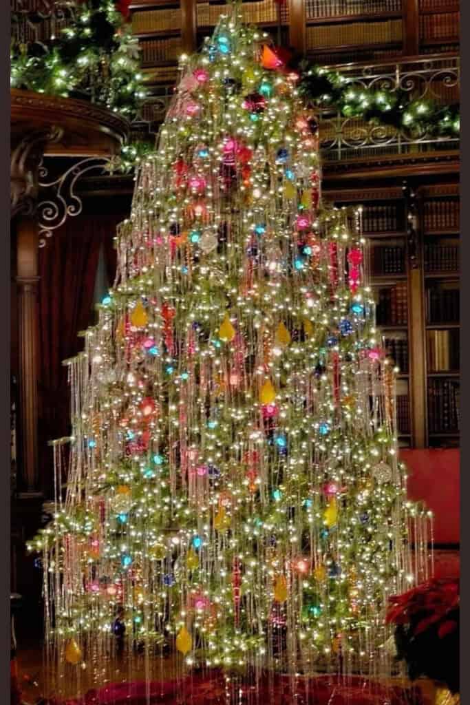 Vintage 80s-inspired Christmas tree decorated with silver tinsel, colorful lights, and retro ornaments in an elegant, old-world library.