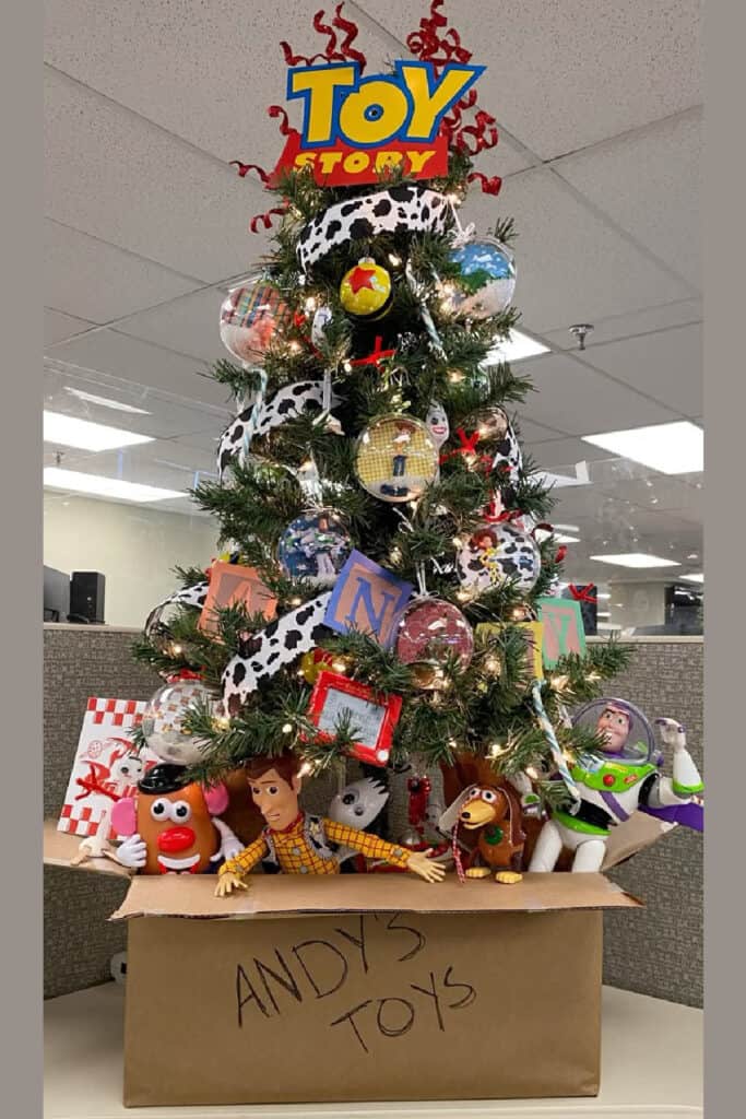 Whimsical Toy Story-themed Christmas tree decorated with character ornaments, cow-print ribbon, alphabet blocks, and topped with a Toy Story logo. The base features a box labeled "Andy's Toys" filled with Woody, Buzz Lightyear, Mr. Potato Head, and other Toy Story characters, as part of the whimsical section in a Christmas Decor Ideas 2025 Trends post.