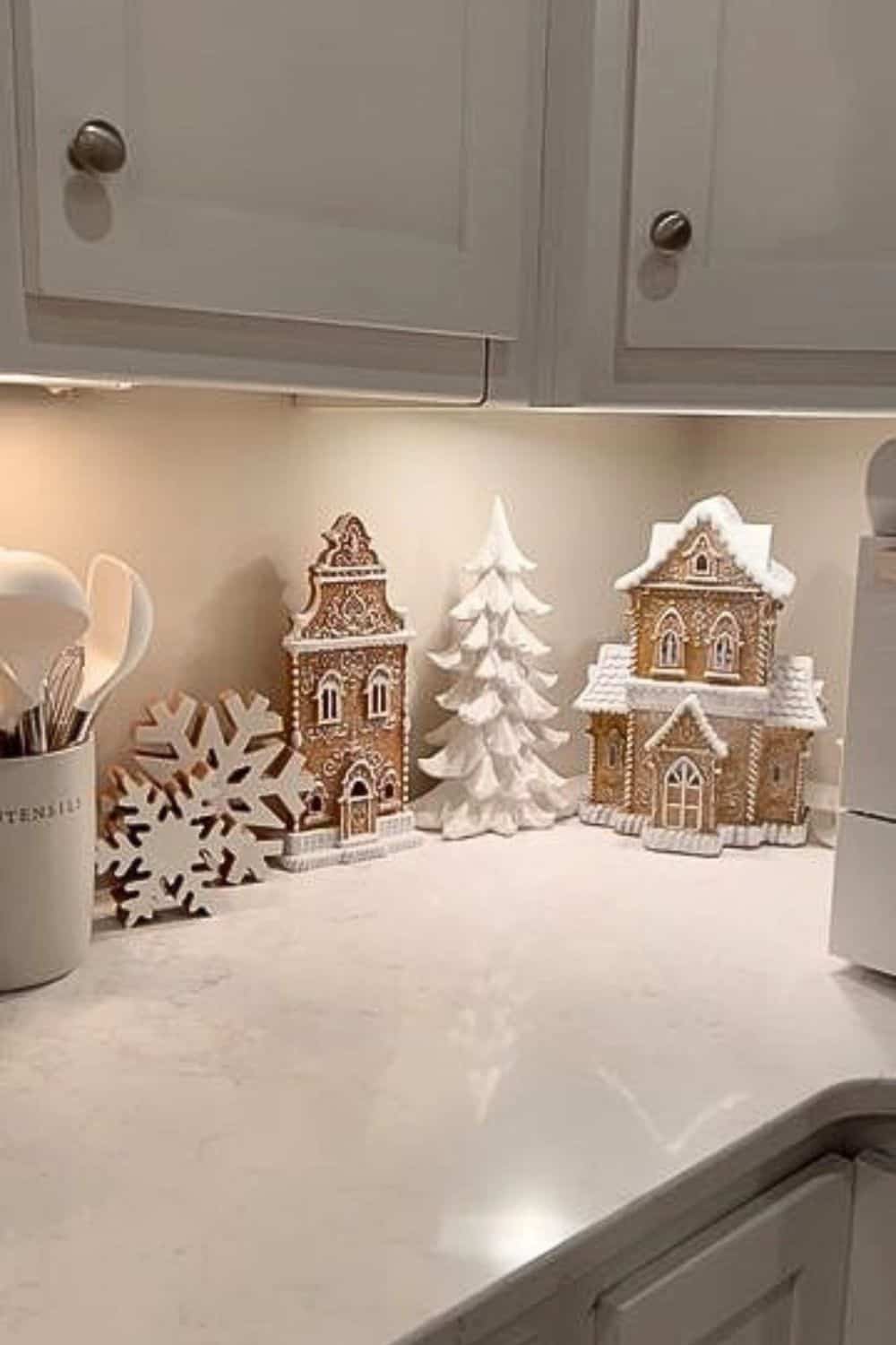 Christmas kitchen counter decorated with gingerbread houses, white holiday tree, and snowflake accents — part of the gingerbread decor trend this year.