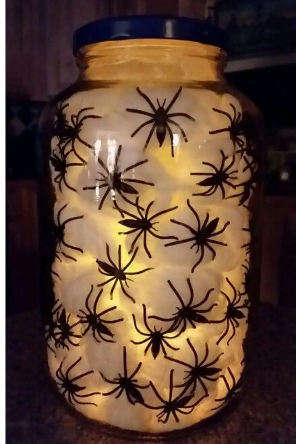 DIY Halloween spider jar light made with a glass jar, fake spiders, cotton, and LED lights — a 15-minute dollar store craft for spooky home decor.