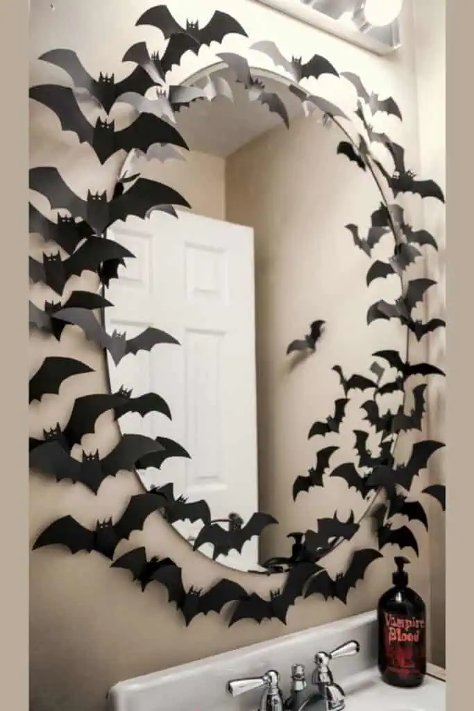 DIY Halloween bathroom mirror decorated with black paper bats and a “Vampire Blood” soap bottle on the sink.