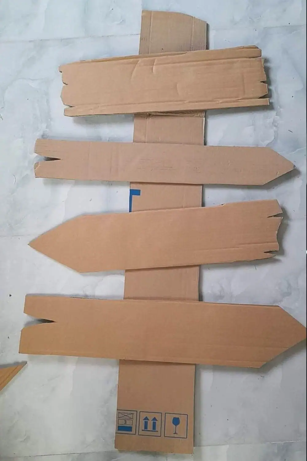Unpainted cardboard arrows stacked on a tall post to make a spooky Halloween directional sign—easy DIY decoration for the yard, porch, or party.