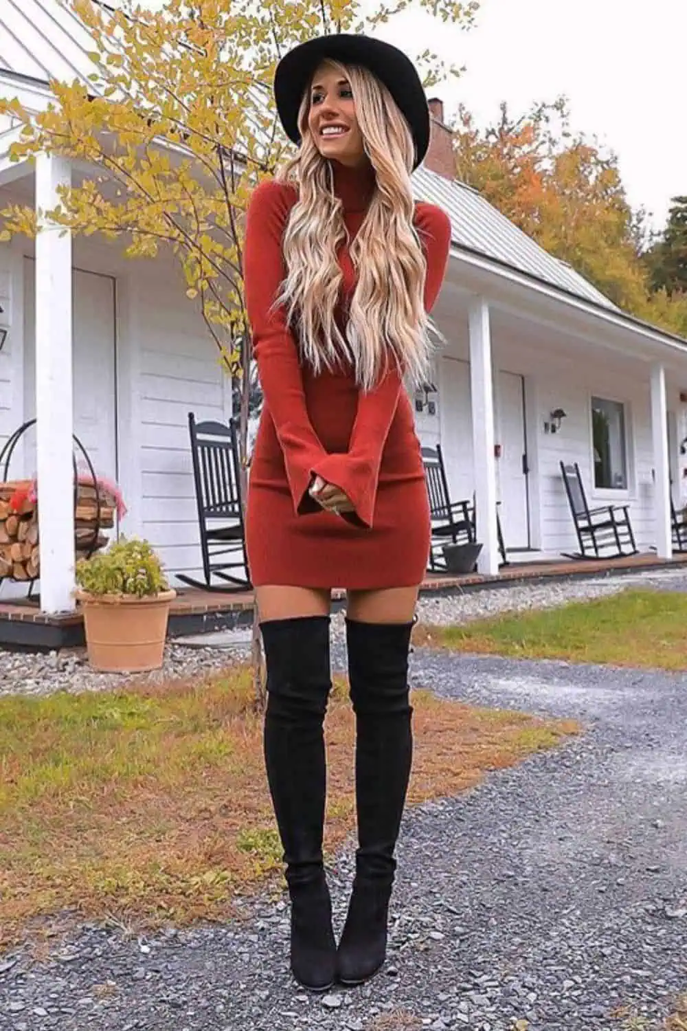 Woman wearing a rust-orange sweater dress and black over-the-knee boots, styled with a wide-brimmed black hat for a cozy and chic fall outfit.