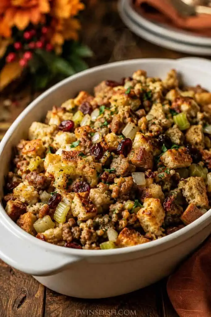Homemade Thanksgiving stuffing in a white casserole dish with toasted bread cubes, sausage, celery, onions, parsley, and dried cranberries.