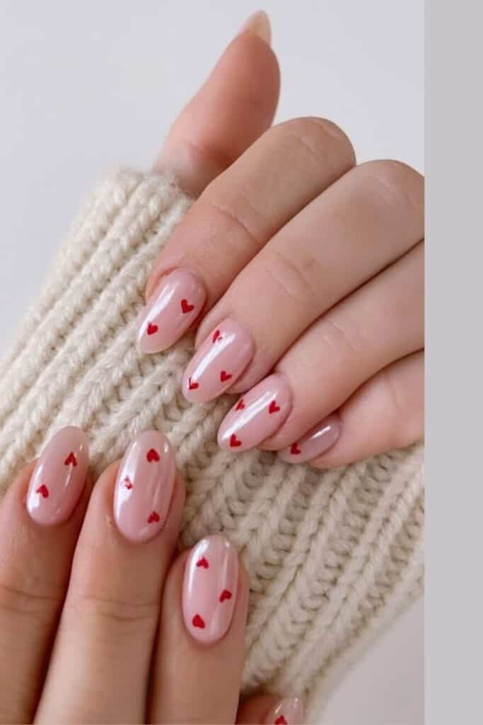 Pink glazed Valentine’s Day nails with small red heart designs on almond-shaped nails