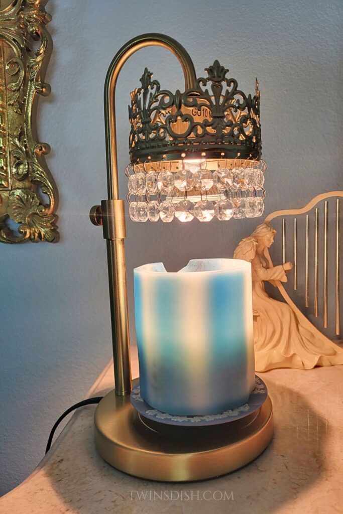 Brass candle warmer lamp with crystal shade warming a blue candle on a side table for cozy apartment decor.