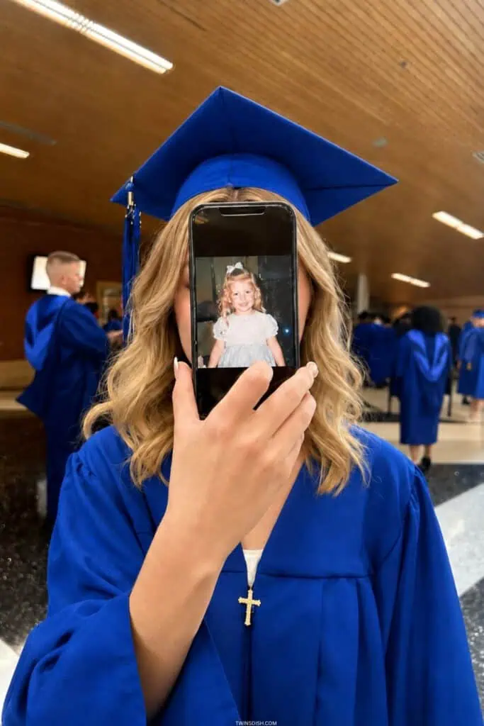 College graduate in blue cap and gown holding phone with childhood photo for college graduation pictures ideas